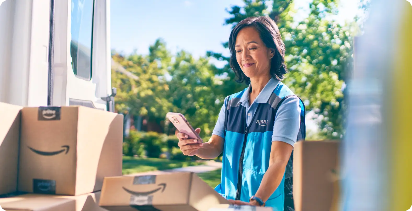 Amazon delivery worker scanning packages outside a delivery van on a sunny day.